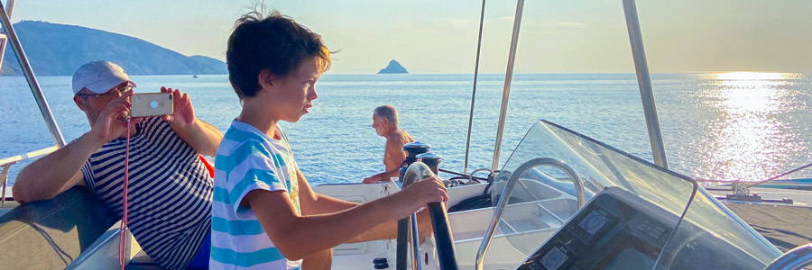 jeune garçon à la barre d'un catamaran en grèce
